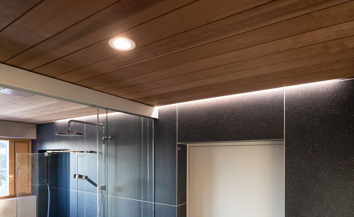 L'area della sauna è illuminata da faretti incassati nel soffitto e da strisce LED indirette lungo la parete accanto al soffitto.